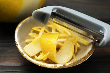 Fresh lemon zest and peeler on wooden table, closeup