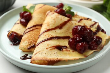 Delicious crepes served with cherry jam and chocolate on white table, closeup