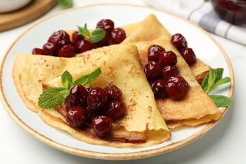 Delicious crepes served with cherry jam on white table, closeup
