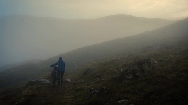 Solitary Cyclist Rides Across Snowy Moorland At Dusk, Low Angle Through Tall Brown Grasses With Snow Patches,
