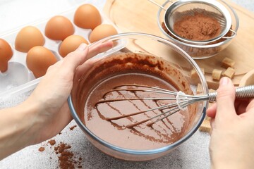 Woman mixing chocolate dough with whisk at grey textured table, closeup
