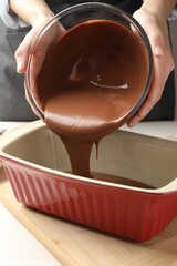 Woman pouring liquid chocolate dough into baking dish at table, closeup
