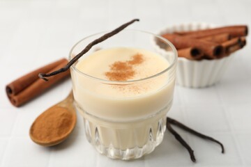 Delicious protein shake in glass, cinnamon and vanilla pods on white tiled table, closeup