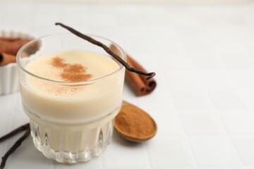 Delicious protein shake in glass, cinnamon and vanilla pods on white tiled table, closeup. Space for text