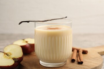 Delicious protein shake in glass, apples, cinnamon and vanilla pods on table, closeup