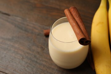 Delicious protein shake in glass, cinnamon and banana on wooden table, closeup. Space for text