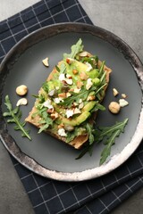 Tasty bruschetta with avocado, arugula, nuts and feta cheese on grey table, top view