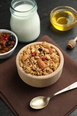 Tasty granola with dried fruits, nuts, honey and milk on black table, closeup