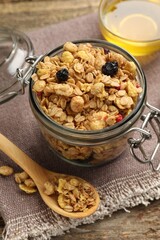 Tasty granola with dried fruits in glass jar and honey on wooden table, closeup