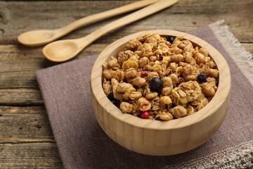 Tasty granola with dried fruits in bowl and spoons on wooden table, closeup