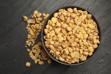Tasty granola with dried fruits in bowl on black table, top view