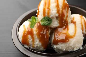 Tasty ice cream with caramel sauce and mint in bowl on black table, closeup