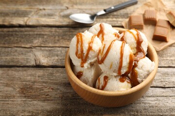 Tasty ice cream with caramel sauce in bowl on wooden table, closeup. Space for text