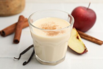 Delicious protein shake in glass, cinnamon, apples and vanilla pods on white table, closeup
