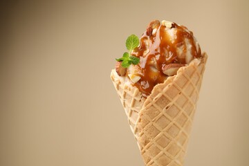Tasty ice cream with caramel sauce, almonds and mint on beige background, closeup. Space for text