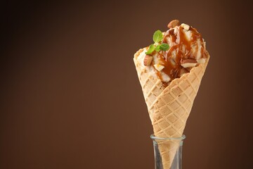 Tasty ice cream with caramel sauce, almonds and mint on brown background. Space for text
