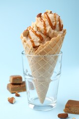 Tasty ice cream with caramel sauce and almonds on light blue background