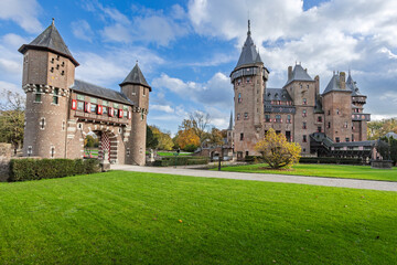 Entrance gatehouse and drawbridge of Castle De Haar. Medieval brick architecture with towers, shutters, and green lawn on a sunny day.