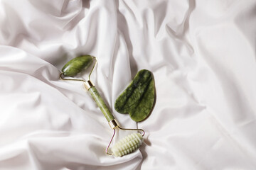 Jade facial roller and gua sha tool on minimalist white satin background