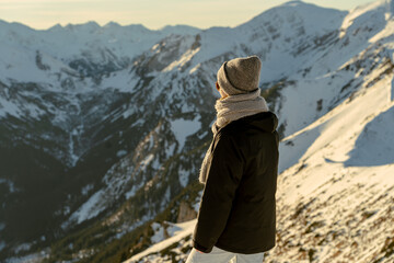 Person stands on mountain peak looking at snow-covered landscape during sunset in winter season © Strikernia