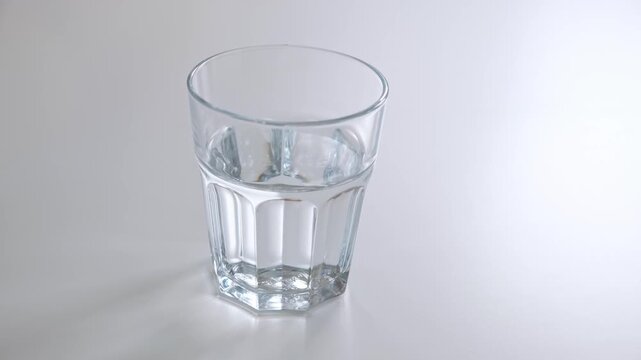 One glass of water is on the white table side view. Concept of morning routine, morning ritual, mindful living. Everyday action. Healthy lifestyle. High quality 4k footage.