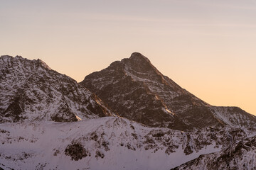 Snow-covered mountain peak during sunset with clear skies in the background near a snowy landscape
