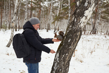 Man feeds squirrel while standing by tree in snowy forest during winter