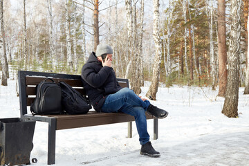  A man sits on a wooden bench in a snowy park and talks on a telephone