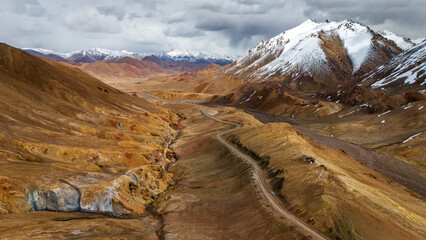 aerial high-altitude mountain pass on the Pamir Highway (M41). Remote, rugged gravel road winding through the vast, arid landscape of the Pamir Mountains in Tajikistan, near the Ak-Baital Pass (4655m)