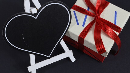 Biglietto di auguri per San Valentino con cuore nero, confezione regalo con fiocco rosso su sfondo nero.