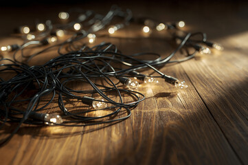 Tangled Christmas string lights lying on a wooden floor with warm glowing bulbs. Cozy winter atmosphere, soft light and shallow depth of field, minimal holiday concept.