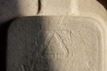 Detailed macro shot of an industrial recycled paper or fiber egg carton, emphasizing the universal recycling logo and the textured, natural, and earthy brown surface. Ideal for eco-conscious designs.