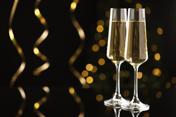 Merry Christmas and Happy New Year. Flute glasses with sparkling wine and serpentine streamers on black background against blurred lights. Space for text