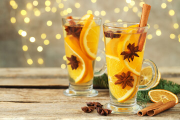 Delicious mulled wine with slices of orange, spices and fir branches on wooden table against grey background with blurred Christmas lights, closeup with space for text. Bokeh effect