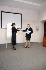 Fototapeta premium Two businesswomen shaking hands after a presentation in an office with flip chart, business meeting, partnership and success