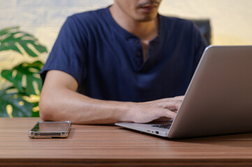 Person Working on Laptop with Smartphone on Wooden Desk Background