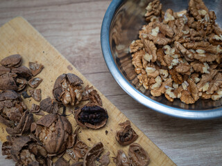 Cracked walnuts on a wooden board with one spoiled dark kernel caused by improper drying or rot, next to a bowl of healthy walnut kernels. Food quality control, defect comparison, storage problem.
