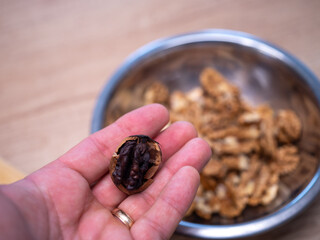Human hand holding a spoiled walnut kernel with signs of rot and improper drying, cracked shell visible. Close up of food defect, quality problem, mold risk, bad storage and unhealthy nut concept.