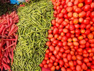 Fresh vegetables piled at market stall with red carrots, green beans and ripe tomatoes