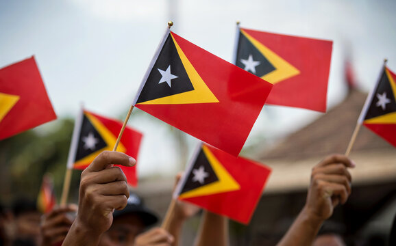 Hands Holding Small Timor-Leste National Flags Waving for Independence Day Celebration - Powered by Adobe