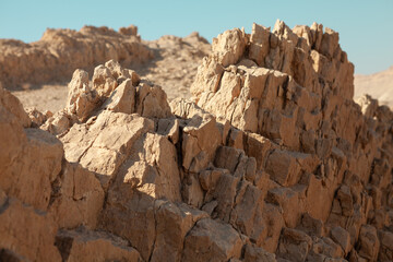 Close-up shot of sharp, jagged, sun-drenched sedimentary rock formations, possibly ancient sea bed remnants, under a clear blue sky in a desert landscape near Qom, Iran.