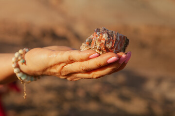 Close-up of a woman's hand holding a colorful mineral rock outdoors in warm sunlight. The natural stone displays layered textures and earthy tones, symbolizing geology, nature, and exploration.