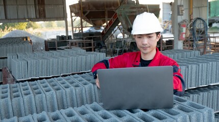 A foreman carefully inspects concrete blocks at a construction site while using a laptop to ensure compliance with construction standards.