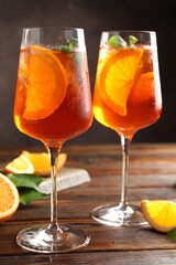 Glasses of refreshing spritzer cocktail and oranges on wooden table