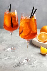 Glasses of refreshing spritzer cocktail and oranges on grey textured table