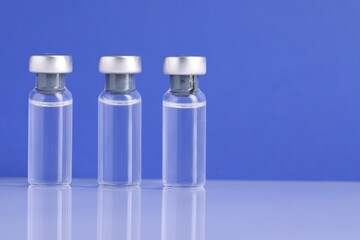 Vaccine in vials on light mirror surface against blue background, closeup. Space for text