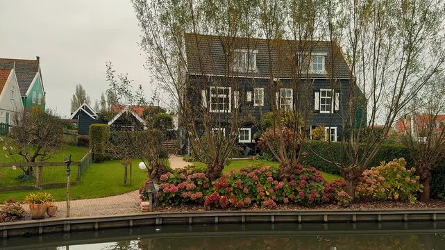 Panoramic view of Marken, Netherlands, featuring traditional green wooden houses, a classic white drawbridge, and a calm canal reflecting the overcast sky during a cloudy day.

