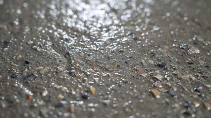 Wet asphalt road surface with small stones and pebbles reflecting light