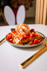 Waffle dessert with vanilla ice cream, strawberries, and caramel sauce on a clean white table....