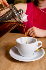 Tea being poured into a white cup from a glass teapot. Warm tones, cozy café mood, and lifestyle composition with hands create an inviting drink moment